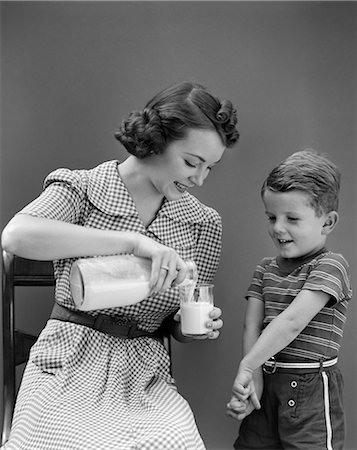 ANNÉES 1940 FEMME MÈRE ASSISE COULÉE DE VERRE DE LAIT POUR FILS GARÇON DEBOUT À CÔTÉ D'ELLE Photographie de stock - Rights-Managed, Code: 846-06111810