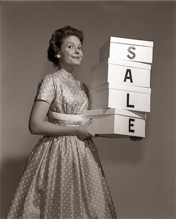 1960s WOMAN IN POLKA-DOT DRESS LOOKING AT CAMERA HOLDING A STACK OF 4 BOXES WITH ONE CHARACTER CENTERED ON EACH SPELLING SALE Foto de stock - Con derechos protegidos, Código: 846-06111845