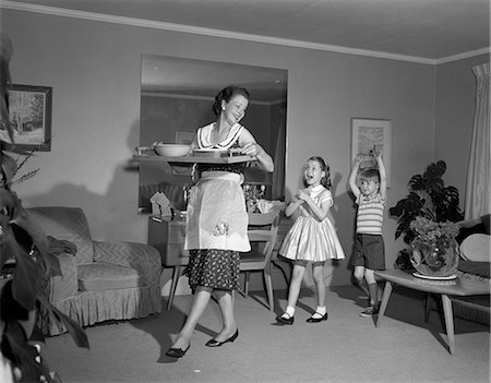 1960s MOTHER WALKING WITH TRAY OF SNACK FOOD HAPPY SON AND DAUGHTER FOLLOWING HER INDOOR Stock Photo - Rights-Managed, Code: 846-06111927