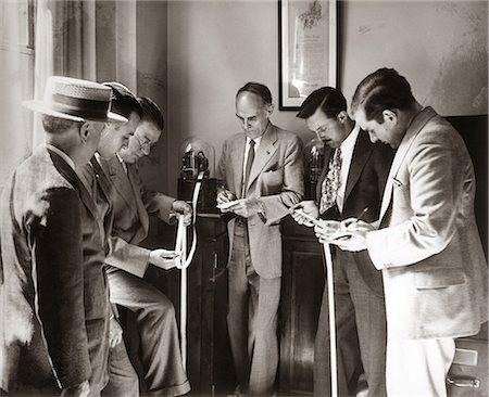 1930s BROKERS BUSINESSMEN READING TICKER TAPE AS IT COMES OUT OF GLASS DOMED MACHINE Stock Photo - Rights-Managed, Code: 846-06112288