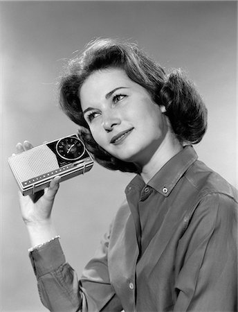 1960s PORTRAIT OF SMILING TEENAGE GIRL TILTING HEAD TO LISTEN TO PORTABLE RADIO HELD IN HAND TO EAR Foto de stock - Con derechos protegidos, Código: 846-06112371