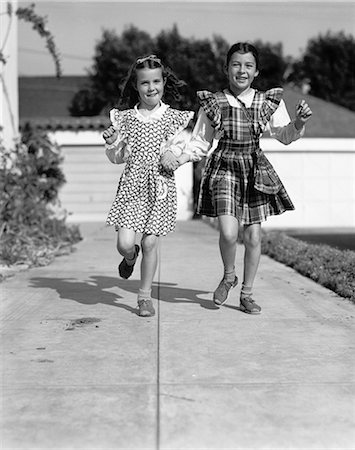 simsearch:846-08512702,k - 1930s 1940s TWO GIRLS SKIPPING  DOWN SIDEWALK HOLDING  HANDS LOOKING AT CAMERA Stock Photo - Rights-Managed, Code: 846-07200063