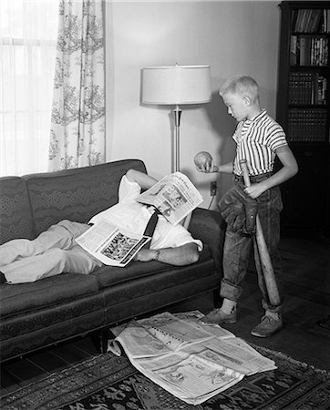1950s FATHER LYING ON A SOFA WITH NEWSPAPER OVER HIS HEAD WHILE SON IS STANDING OVER HIM WITH BAT BALL AND BASEBALL GLOVE Photographie de stock - Rights-Managed, Code: 846-07200084