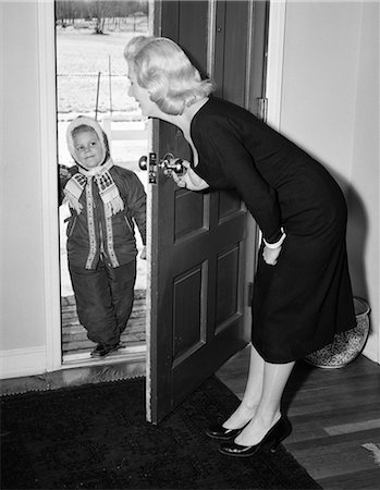 1950s BLONDE MOM OPENING FRONT DOOR TO LET IN CHILD DRESSED WINTER SNOW SUIT SCARF HAT CAN SEE SNOW SCENE THROUGH DOOR Foto de stock - Con derechos protegidos, Código: 846-07200086