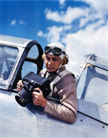 1940s ARMY AIR CORPS MAN SITTING AIRPLANE COCKPIT WEARING FLYING GOGGLES HELMET PARACHUTE TAKING PHOTOGRAPHS WITH AERIAL CAMERA Photographie de stock - Rights-Managed, Code: 846-07200103