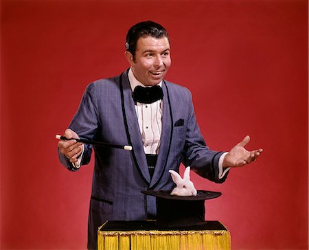 eccentric hat - 1970s MAN MAGICIAN WAVING WAND OVER TOP HAT INVERTED ON TABLE WHITE RABBIT APPEARS Stock Photo - Rights-Managed, Code: 846-07760714