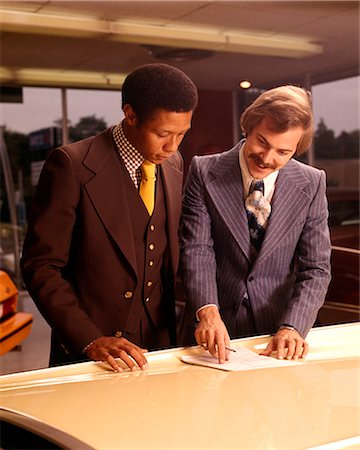 1970s TWO MEN CUSTOMER AND SALESMAN READING SALES CONTRACT ON HOOD OF NEW CAR IN DEALERSHIP SALES SHOWROOM Photographie de stock - Rights-Managed, Code: 846-07760725