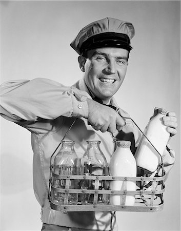 simsearch:846-08226149,k - 1950s 1960s SMILING MILKMAN IN UNIFORM LOOKING AT CAMERA CARRYING TWO FULL AND TWO EMPTY BOTTLES OF MILK IN METAL CARRIER Stockbilder - Lizenzpflichtiges, Bildnummer: 846-07760761