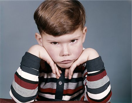 1960s PORTRAIT SAD ANGRY LITTLE BOY STRIPED SHIRT FACE RESTING IN HIS HANDS LOOKING AT CAMERA Stock Photo - Rights-Managed, Code: 846-08030391