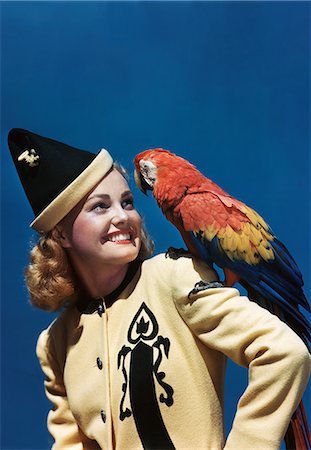 papagaio (pássaro) - 1940s SMILING BLOND WOMAN WEARING YELLOW AND BLACK JACKET AND POINTED HAT LOOKING AT PARROT ON SHOULDER Foto de stock - Direito Controlado, Número: 846-08030408