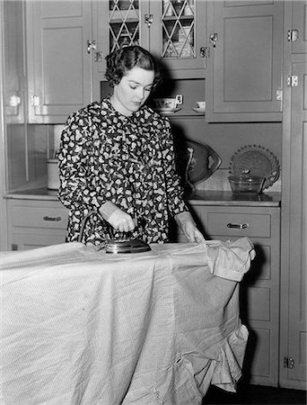 electric appliance - 1930s 1940s WOMAN WEARING PRINTED SMOCK APRON STANDING IRONING BOARD PUSHING ELECTRIC IRON Photographie de stock - Rights-Managed, Code: 846-08140042