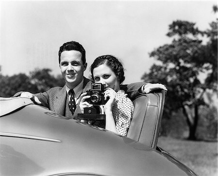 1930s COUPLE SITTING IN JUMP SEAT OF CAR POINTING CAMERA AT VIEWER Foto de stock - Con derechos protegidos, Código: 846-08140084