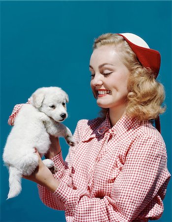 1940s 1950s PORTRAIT SMILING BLOND TEEN GIRL WEARING RED AND WHITE CHECKED BLOUSE AND DUTCH STYLE HAT HOLDING WHITE SPITZ PUPPY Foto de stock - Con derechos protegidos, Código: 846-08140087