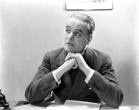 1930s 1940s MAN PORTRAIT AT DESK BUSINESSMAN WEARING SUIT HANDS CLASPED UNDER CHIN LOOKING OFF TO SIDE Foto de stock - Con derechos protegidos, Código: 846-08140098