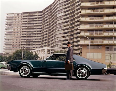 simsearch:846-08226149,k - 1960s SALESMAN WITH ATTACHÉ CASE STANDING BESIDE OLDSMOBILE TORONADO CAR OUTSIDE APARTMENT CONDOMINIUM BUILDING Stockbilder - Lizenzpflichtiges, Bildnummer: 846-08226133