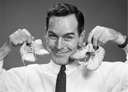 simsearch:846-03165114,k - 1950s SMILING PORTRAIT MAN HOLDING ONE PAIR OF BABY BOOTIES IN EACH HAND NEXT TO FACE Stockbilder - Lizenzpflichtiges, Bildnummer: 846-08226144