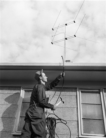 1950s 1960s MAN WORKER ON LADDER RUNNING TELEVISION CABLE TO ANTENNA ON ROOF OF HOUSE Photographie de stock - Rights-Managed, Code: 846-08226151
