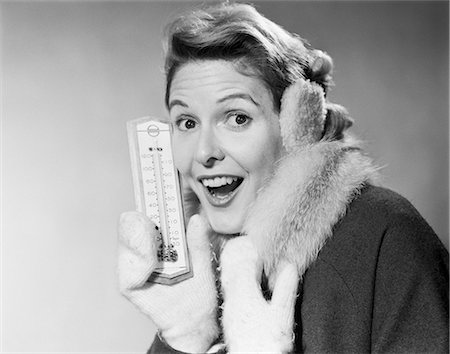 1950s SMILING WOMAN LOOKING AT CAMERA IN WINTER COLD HOLDING THERMOMETER WEARING COAT MITTENS EARMUFFS Foto de stock - Con derechos protegidos, Código: 846-08512695