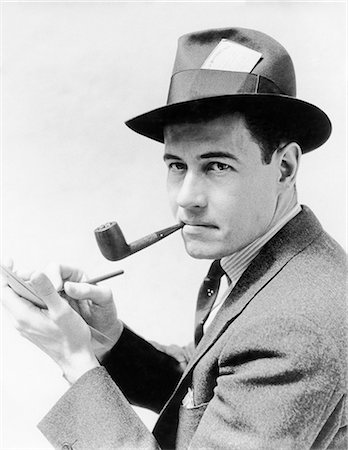 1930s 1940s MAN REPORTER WEARING HAT WITH PRESS PASS WRITING NOTES IN PAD TABLET SMOKING PIPE LOOKING AT CAMERA Stock Photo - Rights-Managed, Code: 846-08512746