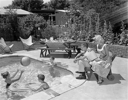 1950s 1960s BACKYARD PATIO POOL PARENTS MOTHER FATHER MAN WOMAN SEATED WATCHING THREE CHILDREN PLAYING IN WATER Foto de stock - Con derechos protegidos, Código: 846-08512752