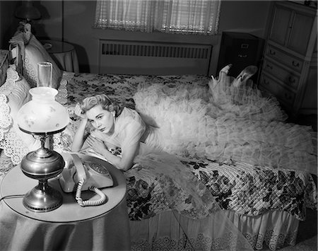 1950s SAD BLOND WOMAN LOOKING STOOD UP WEARING CHIFFON RUFFLED EVENING GOWN LYING ON BED WAITING BY TELEPHONE Foto de stock - Con derechos protegidos, Código: 846-08639579