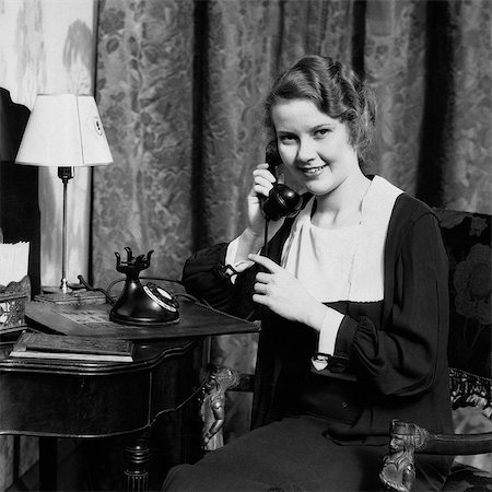 1930s SMILING WOMAN SITTING AT DESK VANITY TABLE WITH MIRROR LAMP STATIONARY TALKING ON TELEPHONE LOOKING AT CAMERA Stock Photo - Rights-Managed, Code: 846-08639584