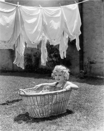 1930s 1940s GIRL OUTDOORS SITTING IN LAUNDRY BASKET UNDER CLOTHESLINE FULL OF SHIRTS Stock Photo - Rights-Managed, Code: 846-08721100