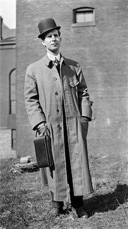 1900s 1910s PORTRAIT MAN STANDING BOWLER HAT LONG WOOL COAT LOOKING AT CAMERA HOLDING LEATHER CASE POSTCARD SIZE KODAK CAMERA Foto de stock - Direito Controlado, Número: 846-08721119