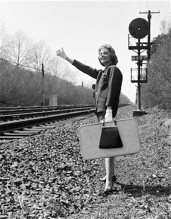 suitcase walking away - 1950s 1960s WOMAN SMILING HOLDING SUITCASE STANDING BESIDE RAILROAD TRACKS GLOVED HAND THUMB IN THE AIR TO HITCH A RIDE Stock Photo - Rights-Managed, Code: 846-08721120