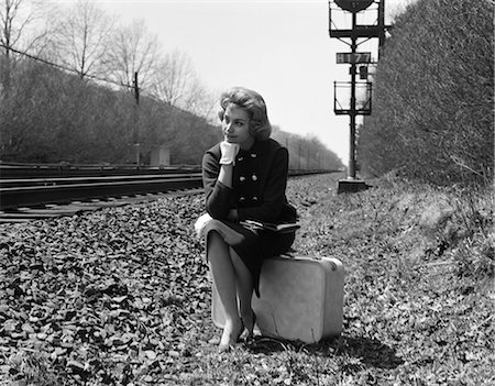 1950s 1960s WOMAN SAD WORRIED FACIAL EXPRESSION SITTING  ON SUITCASE BY SIDE RAILROAD TRACKS Stock Photo - Rights-Managed, Code: 846-08721121