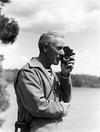 simsearch:846-09085274,k - 1930s ELDERLY MAN OUTDOORS BY LAKE HOLDING A SMALL COMPACT 8MM MOVIE CAMERA UP TO HIS EYE Stock Photo - Rights-Managed, Code: 846-08721133