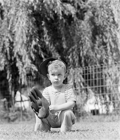 1940s SMALL SERIOUS BLOND BOY HOLDING A BASEBALL MITT WEARING BASEBALL CAP IN THE GRASS Stock Photo - Rights-Managed, Code: 846-09012702