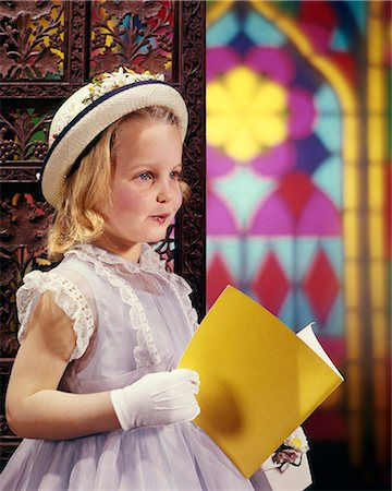 1950s 1960s LITTLE YOUNG GIRL IN CHURCH HAT GLOVES HOLDING YELLOW PRAYER PROGRAM BY STAINED GLASS WINDOW Stockbilder - Lizenzpflichtiges, Bildnummer: 846-09012856