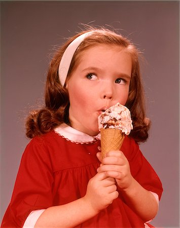 foods kids - 1960s CUTE EXPRESSION BRUNETTE LITTLE GIRL WEARING A RED DRESS EATING ICE CREAM CONE Stock Photo - Rights-Managed, Code: 846-09012889