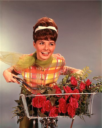 simsearch:846-05646643,k - 1960s SMILING TEEN GIRL WITH TEASED BRUNETTE BOUFFANT HAIRDO RIDING BICYCLE WITH RED ROSES BOUQUET IN BASKET Foto de stock - Direito Controlado, Número: 846-09012895