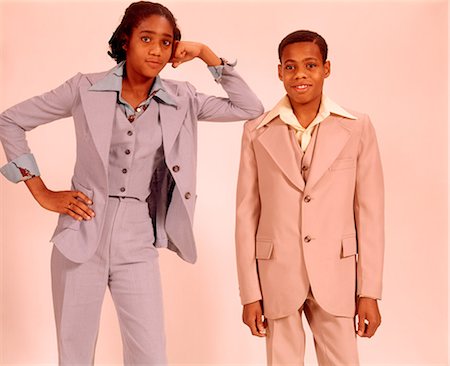 1970s TWO AFRICAN AMERICAN TEENAGERS A BOY IN A BEIGE SUIT AND GIRL IN A BLUE PANTS SUIT STANDING TOGETHER LOOKING AT CAMERA Photographie de stock - Rights-Managed, Code: 846-09012944