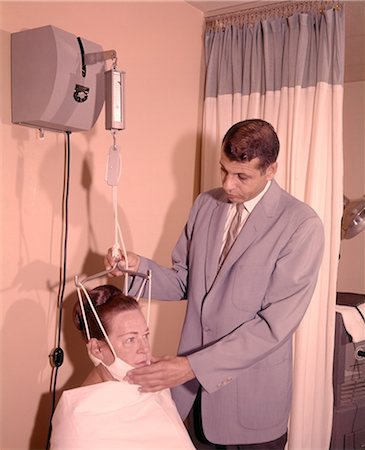 1950s 1960s MAN TECHNICIAN ADJUSTING TENSION ON WOMAN PATIENT CHIN BRACE NECK TRACTION MEDICAL EQUIPMENT Stock Photo - Rights-Managed, Code: 846-09012948