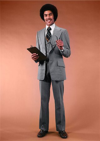 simsearch:846-07760725,k - 1970s AFRICAN AMERICAN MAN BUSINESSMAN SUIT HOLDING GLASSES CLIPBOARD SMILING LOOKING AT CAMERA Stock Photo - Rights-Managed, Code: 846-09012991