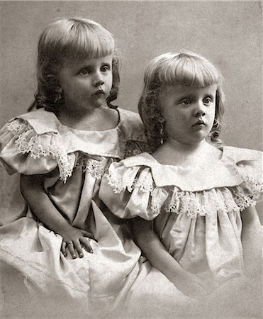 1890s PORTRAIT TURN OF THE 20TH CENTURY TWIN GIRLS SISTERS WEARING IDENTICAL DRESSES AND SHOWING MOROSE SAD FACIAL EXPRESSIONS Stock Photo - Rights-Managed, Code: 846-09013086