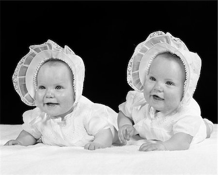 1950s TWIN BABY GIRLS WEARING BONNETS LYING ON THEIR STOMACHS SMILING Foto de stock - Con derechos protegidos, Código: 846-09085261