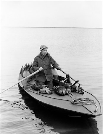 simsearch:6122-07698263,k - 1950s MAN DUCK HUNTER WITH HARVEST ROWING BARNEGAT BAY SNEAK BOX BOAT NEW JERSEY USA Stock Photo - Rights-Managed, Code: 846-09085274