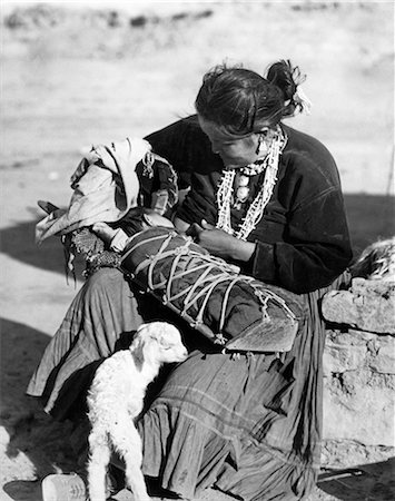 1930s NATIVE AMERICAN NAVAJO WOMAN MOTHER BREAST FEEDING BABY IN PAPOOSE BABY LAMB AT HER FEET Fotografie stock - Rights-Managed, Codice: 846-09085293