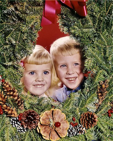 1960s SMILING BLONDE BOY AND GIRL BROTHER AND SISTER PEEKING OUT FROM CENTER OF CHRISTMAS WREATH Stock Photo - Rights-Managed, Code: 846-09085367
