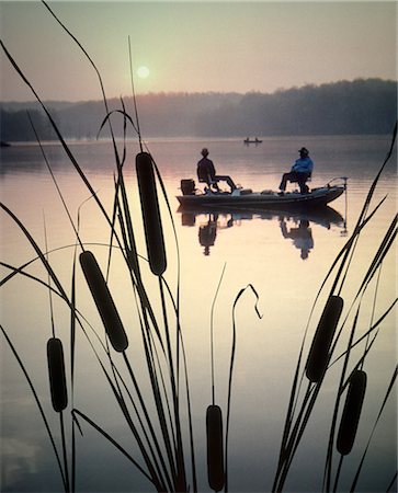 1980s TWO ANONYMOUS SILHOUETTED FISHERMEN SITTING IN MOTOR BOAT FISHING ON LAKE CATTAILS IN FOREGROUND Foto de stock - Con derechos protegidos, Código: 846-09161446