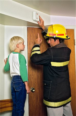 MAN FIREFIGHTER IN PROTECTIVE HELMET AND TURNOUT JACKET INSTRUCTING YOUNG BLOND BOY ABOUT HOME SMOKE DETECTOR FIRE ALARM Foto de stock - Con derechos protegidos, Código: 846-09161481