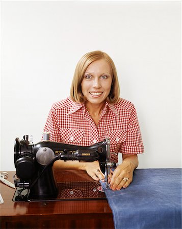 1970s WOMAN HOUSEWIFE OPERATING SEWING MACHINE APPLIANCE HOUSEHOLD SEW CRAFT WEARING CHECKED BLOUSE LOOKING AT CAMERA Stock Photo - Rights-Managed, Code: 846-09161527