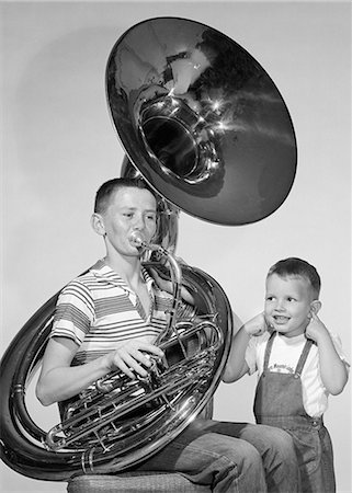 1950s TEEN BOY IN STRIPE SHIRT JEANS PLAYING TUBA SMALLER BROTHER IN BIB OVERALLS SMILING INDEX FINGERS STUCK IN BOTH EARS Stockbilder - Lizenzpflichtiges, Bildnummer: 846-09161559