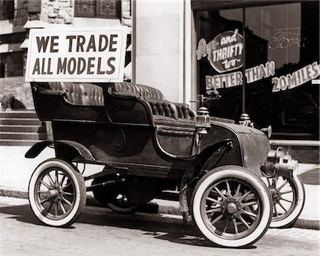 ford - 1930s ANTIQUE CAR WITH WE TRADE ALL MODELS ADVERTISING SIGN PARKED ON STREET IN FRONT OF CAR DEALERSHIP Stockbilder - Lizenzpflichtiges, Bildnummer: 846-09161560