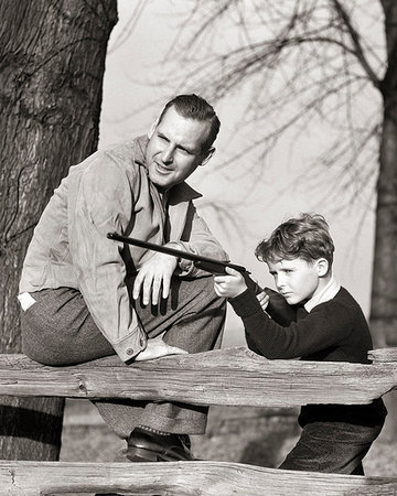 family life 1930s - 1930S FATHER TEACHING SON FIREARM FUN SAFETY BOY AIMING RIFLE OVER A WOODEN FENCE DAD SITTING ON FENCE Photographie de stock - Rights-Managed, Code: 846-09181494