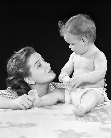 1940s ALERT BABY DAUGHTER SITTING UPRIGHT LOOKING FACE TO FACE AT EXPRESSIVE MOTHER WHO IS PINCHING HER FOOT Photographie de stock - Rights-Managed, Code: 846-09181574
